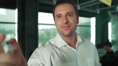 Akıllı lider iş adamı cam tahtanın önünde projeyle ilgili yazı yazıyor. Gülümseyen erkek proje yöneticisi fikir paylaşımı, yapışkan notlar üzerine plan yaratıcılık pazarlama stratejisini gösteriyor. Yönlendirici.