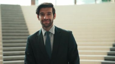 Akıllı iş adamı merdivenlerde kameraya bakıyor. İş elbisesi giyerken kameraya gülümseyen başarılı adamın yakın çekimi. Yönetici, kameraya bak. Hareket eden kamera. Sevinçli..