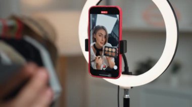 Arka plan etkileyicisi, vlog video gözden geçirme makyaj primi sosyal medya ya da blog kullanarak akıllı telefon yayınıyla canlı çekim yapıyor. İnternetteki pazarlama kaydı için kozmetik stüdyosu ışıklandırması olan kız.