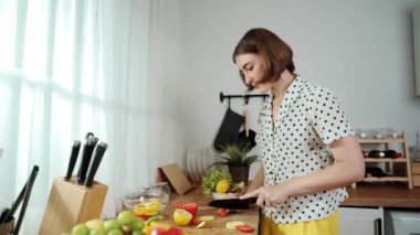 Enerjik anne, mutfak malzemeleri ile çevrili sebzeleri doğrarken modern mutfakta kahvaltı için salata yapıyor. Akıllı kadın temizlikçi yemek pişirir ve yemek hazırlar. Sağlıklı bir yaşam tarzı. Pedagoji.