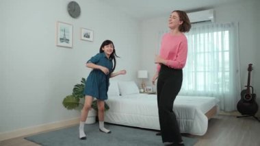 Yatak odasında Asyalı kızıyla müzik eşliğinde dans eden mutlu çekici anne. Beyaz anne dans eder ya da egzersiz yapar. Bu arada tatlı çocuk da müzik eşliğinde yatağa atlar. Aile eğlence konsepti. Pedagoji.