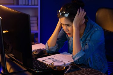 Stresli, genç, güzel Asyalı yaratıcı proje yaratıcısı sosyal medyayı araştırmak için bilgisayara bakıyor ve geceleri daha çok neon modern ofisin planlama kanalı stratejisine ulaşılıyor. Taktik.