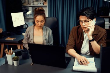 Satış müdürünün dizüstü bilgisayarında çalışan ciddi bir yüz sekreterli müşteriyi arıyor ve modern ofiste gece geç saatlerde evrak işleri ile ilgili notlar yazıyor. Aşırı çalışan problem projesi kavramı. İnfobahn.