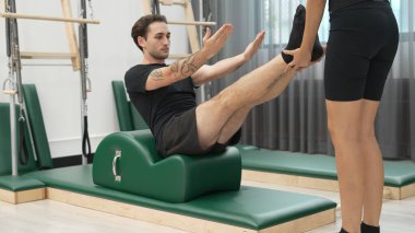 Erkek müşteri pilates ark fıçısında bacak kaldırma alıştırması yapıyor. Vücut dengesini, bacak dayanıklılığını ve spor salonundaki esnekliğini arttırmak için eğitmen yardımı ile birlikte. Öğrenci yalancı ve muziplik pozu veriyor. Alışkanlık.