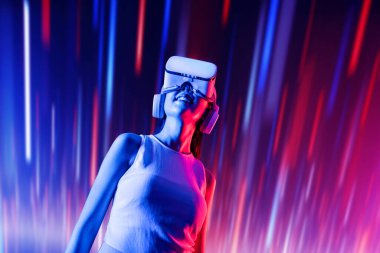 Zeki bir kadın, metaevreni birbirine bağlayan VR kulaklık takan neon ışıklarla çevrili duruyor. Gelecekteki siber uzay topluluğu teknolojisi. Uzaklara bakan zarif bir kadın ve tatmin edici bir şekilde gülümsüyor. Halüsinasyon.