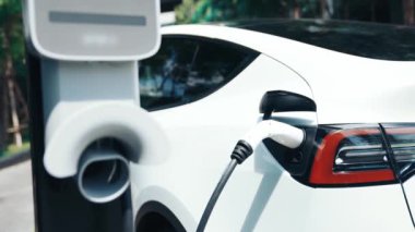 Yavaş çekim EV elektrikli araba yazın yeşil sürdürülebilir şehir parkı bahçesinde şarj oluyor. Elektrikli araç iç organları için kentsel yaşam tarzında sürdürülebilir temiz şarj edilebilir enerji