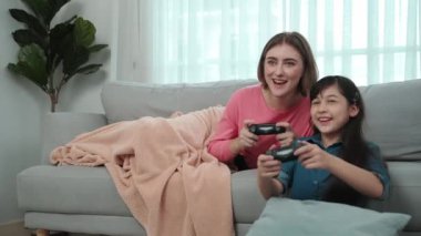 Annem kanepede yatarken, mutlu kız oyun oynuyor ve oturuyor. Beyaz bir ebeveyn ve çekici zeki bir kız elinde joystick ile birlikte vakit geçirip maç kazanmaya odaklanıyor. Yaşam tarzı. Pedagoji.