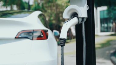 Yavaş çekim EV elektrikli araba yazın yeşil sürdürülebilir şehir bahçesinde şarj oluyor. Kentsel sürdürülebilirlik yaşam tarzı yeşil temiz yeniden şarj edilebilir enerji elektrikli BEV araç iç organları