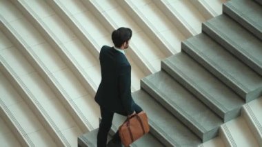 Akıllı bir iş adamının elinde çantayla merdivenlerden yukarı çıkışının en üst görüntüsü. Profesyonel proje yöneticisi merdivenlerden çıkıp işyerine gidiyor. Yeteneklerini arttırmak, terfi almak, seyahat etmek. Sevinçli..