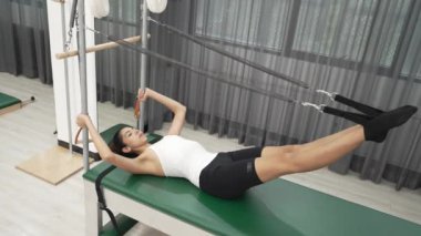 Kadın spor salonunda vücut ve bacak gücünü arttırmak için trapez masasında pilates bacak egzersizi yapıyor. Kalça esnekliğini arttırmak için Cadillac 'ın kayışıyla bacak uzatma ameliyatı yapan mutlu antrenör. Alışkanlık.