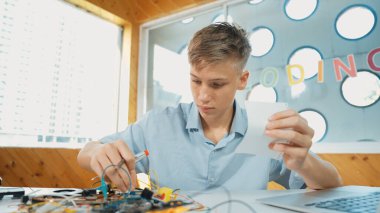 Akıllı çocuk notlara bakarken elektronik alet kullanmayı öğrenir ya da inceler. Lise öğrencisi STEM teknoloji sınıfında otururken elektrikli aletler üzerinde çalışıyor ya da teftiş yapıyor. Öğretim.