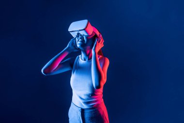 Siberpunk neon ışıklı cihazlarla çevrili zeki bir kadın metaevrene bağlı VR kulaklık takıyor, gelecekçi siber uzay teknolojisi. Zarif bir kadın sanal ortamda yaratılmış gibi görünür. Halüsinasyon.