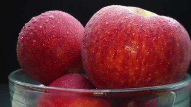 Yakın plan vitrinlerde cam bir kaseye yerleştirilmiş taze kırmızı bir elma görülüyor. Siyah arkaplan, elmaların kusursuz ve pürüzsüz cildini vurgulayan dramatik bir sahne yaratıyor. Geliştirilebilir.