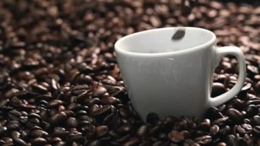 Kahve fincanının içine kahve çekirdeği yığını ile çevrili bir şekilde düşüyor. Beyaz fincana aromatik fasulye döküyorum. Kahvenin üst görüntüsü siyah arka planlı cama düşer. Geliştirilebilir.
