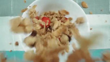 Sağlıklı bir mısır gevreği ve kuru çilek tabağına yakın durun. Yukardan aşağıya mısır gevrekli kase, mavi ve beyaz peçeteli kuru meyve. Makrografi. Ağır çekim. Kahvaltıda. Pabulum.
