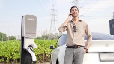 Elektrik şebekesine bağlı elektrik santraline bağlı EV araba aküsünü elektrik endüstrisi için elektrik endüstrisi olarak şarj eden yavaş çekim genç adam. Yararlı