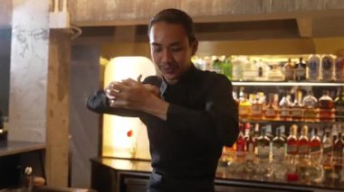 Yakın plan Asyalı barmen, lüks tezgahta karışık kokteyl sallayarak kamera önüne bakarak özel içecek menüsü hazırlıyor. Gece hayatını gösteren özel bir içecek. Vinosity.