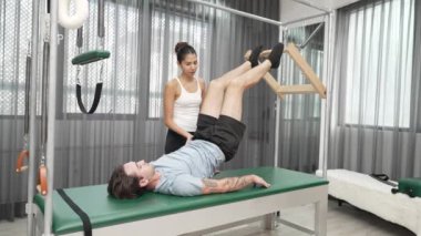 Cadillac ekipmanları üzerinde bacak kaldırma egzersizinde müşteriye yardımcı olan yetenekli pilates eğitmeni. Kadın antrenör, Cadillac 'ın bacak gerdirme hareketine yardım ediyor. Temel bağlantıyı geliştirmek için, bacak esnekliği için. Alışkanlık.