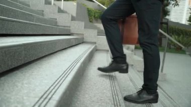 Yakından bakınca iş için çanta tutarken yürüyen zeki bir iş adamının görüntüsü var. Proje yöneticisi çalışmak için merdivenlerden iniyor. Ulaşımı temsil eden, seyahat eden. Bacağa odaklan. Sevinçli..