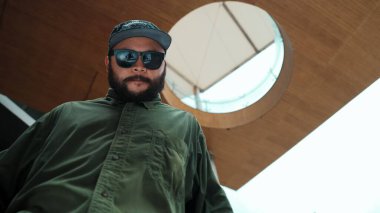 Kameraya bakarken Asyalı yakışıklı hipsterin hip hop pozu. Profesyonel sokak dansçısının alışveriş merkezinde serbest dans edişinin düşük açılı görüntüsü. Açık hava sporu 2024. Hiphop.