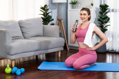 Sportif ve atletik kadınlar spor paspası üzerinde su içiyorlar. Vücut egzersizlerini bitirdikten sonra evde sağlıklı fiziğe ve spor yaşam tarzına uygun bir yaşam sürüyorlar. Gaiety evde egzersiz eğitimi.