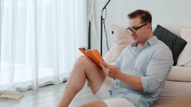 Orta yaşlı bir adam elinde kahve fincanıyla kanepede oturup ders kitabı okuyarak sosyal ve teknolojik meslekler hakkında bilgi artışı yapar ya da çocukları iyi bir yetişkin olarak yetiştirir. Hayat boyu öğrenme konsepti. Uyumsuzluk.