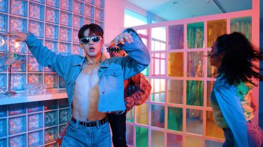 Asyalı adam gece kulübünde çeşitli neon ışıklarda dans ederken kolunu oynatıyor. Modern kulüpte çok kültürlü hippilerle dans eden şık elbiseli mutlu dansçı. Mutluluk.