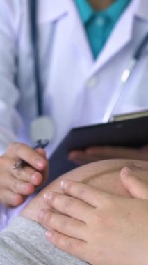 Mutlu hamile kadın, jinekolog doktoru hastanede ya da klinikte hamilelik danışmanlığı için ziyaret ediyor. Doktor, bebek ve anne sağlığı kontrolü için hamile karnı muayene ediyor. Jinekoloji konsepti.