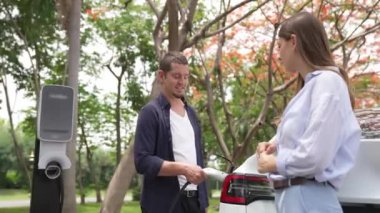 Genç çift sonbaharda ulusal parktaki EV şarj istasyonundan EV elektrikli arabaları şarj ediyor. Tatil ve sonbahar sezonunda çevre dostu arabalarla seyahat. Yararlı