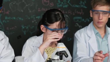 Öğrenci tahtada teoriyle deney yaparken güzel bir kız mikroskop altında araştırma yapıyor. Genç bilim adamı renkli çözeltiyi deneysel ekipmanlarla inceledi. Öğretim