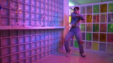 Gece kulübünde kameraya bakarken güneş gözlüklü Asyalı dansçı serbest dans ediyor. Mutlu sokak dansçısı dans ediyor ve renkli parlak neon ışığı ya da yol gösteren ışıkla ayak seslerini gösteriyor. Mutluluk.
