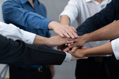 Çeşitli ofis çalışanlarından oluşan bir grup, ofis odasında el ele vererek iş sinerjisini ve iş yerindeki güçlü verimli takım çalışmasını sembolize ediyor. İş çalışanları arasındaki işbirliği ve birlik. Tedbirli