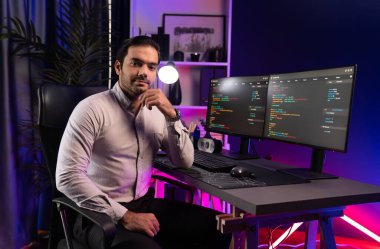 Bilgisayar ekranındaki yazılım geliştirme kodlamasına karşı poz vermek için akıllı bilişim geliştirici görünümlü kamera profilleri, neon ışıklı siber oda ofisinde program güncellemesi internet sitesi verileri sunuyor. Tahmin et..