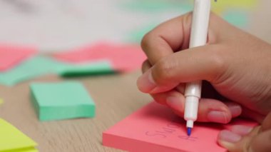 Yavaş çekimde, kadın iş kadını el yazısı pazarlama kâğıdı üzerine kalem ve yapışkan notlarla masaya yerleştirilmiş. Yaratıcı bir girişim ve takım çalışması konsepti. Eline odaklan. Değiştirilmiş.