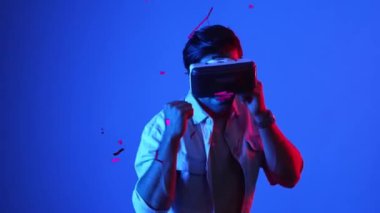 Meta evreni bağlamak için VR gözlük takarken yetenekli oyuncu boksörleri ve yüzen kutuları yumrukluyor. Erkek model, egzersiz yaparken ve neon arka planda dururken sanal gerçeklik gözlüğü kullanıyor. Aygıt.