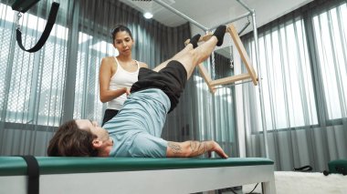 Cadillac ekipmanları üzerinde bacak kaldırma egzersizinde müşteriye yardımcı olan yetenekli pilates eğitmeni. Kadın antrenör, Cadillac 'ın bacak gerdirme hareketine yardım ediyor. Temel bağlantıyı geliştirmek için, bacak esnekliği için. Alışkanlık.