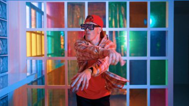 Komik break dansçı kameraya bakarken hiphop 'a doğru serbest adım atıyor. Çılgın mutlu hipster dans edip sokak dansı yaparken Led ışığında günlük kıyafet ve güneş gözlüğü takıyor. Mutluluk.
