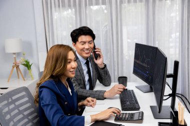 Gülümseyen Asyalı işadamı komisyoncu dinamik borsa veritabanını arıyor. Kadın iş ortağı, iç işyerindeki kar eden uygulama programını karşılaştıran ekranlara işaret ediyor. İnfobahn.