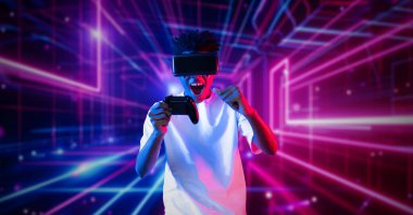 Neon soyut arka planda oyun oynarken elinde joystick tutan ve VR gözlük takan bir genç. Afrikalı adam kontrol etmeyi ve artırılmış gerçeklik teknolojisini kullanmayı seviyor. Yaratıcılık.
