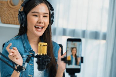 Asyalı sunucu canlı yayında canlı yayında canlı yayında sosyal medyada kulaklık takarak konuşuyor. Dinleyicileri modern stüdyoda koçluk yaparak selamlıyor. Taktik.