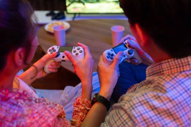Joystickli çiftler arka tarafta oturup video oyunu oynuyorlar. Önden atıştırmalıklar ve modern evdeki neon ışıklı oturma odasında eğlenceli ruh halleri olan içecekler. İnfobahn.