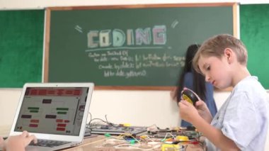 Kafkas arkadaşı STEM sınıfında elektrik panosunu tamir ederken Asyalı çocuk kodlama programı. Enerjik öğrenci kodlama mühendisliği komut yazarken ve yapay zeka yazılımını programlarken tahtada duruyor. Pedagoji.