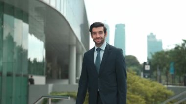 Profesyonel iş adamı hareket ediyor ve kameraya bakarken ayakta duruyor. Gülümseyen yönetici kameraya kendinden emin bir şekilde gülümsüyor. Mimari binada takım elbiseli yatırımcıların yakın çekimi. Sevinçli..