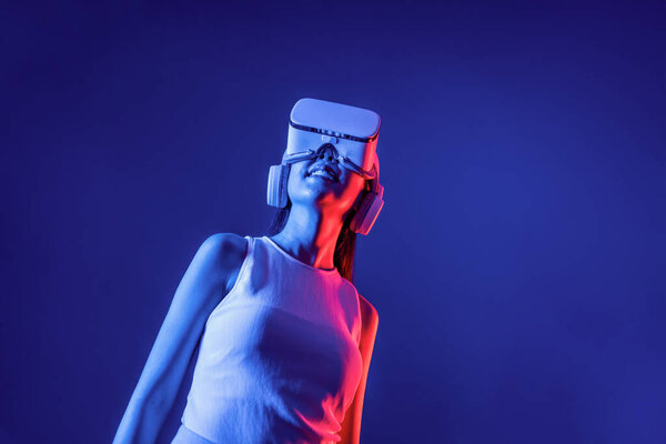 Smart female stand with surrounded by cyberpunk neon light wear VR headset connecting metaverse, futuristic cyberspace community technology. Elegant woman look generated virtual area. Hallucination.