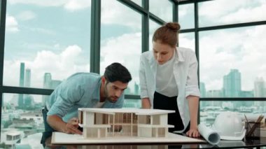 Profesyonel kooperatif iş arkadaşı ev modelini incelerken kalem kullanarak mimari modeli işaret eden yetenekli proje yöneticisi. Mimar mühendis takımı modeli belirlemek için birlikte çalışıyor. İzleme