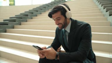 Akıllı telefonlara gülümserken selfie çeken mutlu iş adamı. Profesyonel yöneticinin merdivenlerde takım elbise ve kulaklık takarken görüntüsü. Yaratıcı iş. Sevinçli..