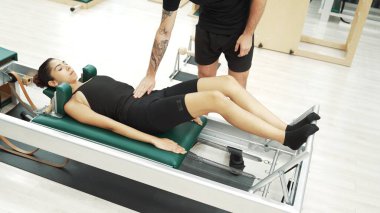 Mutlu pilates eğitmeni, bir müşteriye çekirdek istikrarı geliştirmek için bir reformcu üzerinde bacak egzersizi yapmasında yardımcı oluyor. Pilates makinesi kullanan sportif kız ark fıçısında kol dairesi pozu veriyor. Alışkanlık.