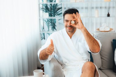 Elinde taze salatalık dilimleri tutan ve bornoz giyen bir adam tatil köyünde ya da otelde yüz bakımının keyfini çıkarıyor. Yüz ve güzellik tedavisi için cilt bakımı. Sessiz.