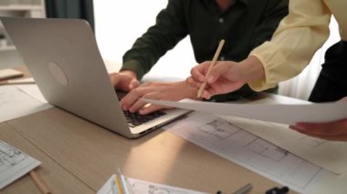 Architect and engineer compare construction detail blueprint display in laptop on table with architectural document or plan and measurement tool for accuracy at modern office. Closeup. Delineation.