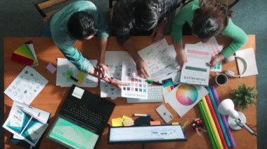 Tasarımcı fikirleri yazarken proje yöneticisinin yukarıdan aşağıya bakan görüntüsü. Akıllı iş adamları logo tasarımı fikrini açıklarken tasarımcılar palete bakarken temayı seçiyorlar. Sempozyum.